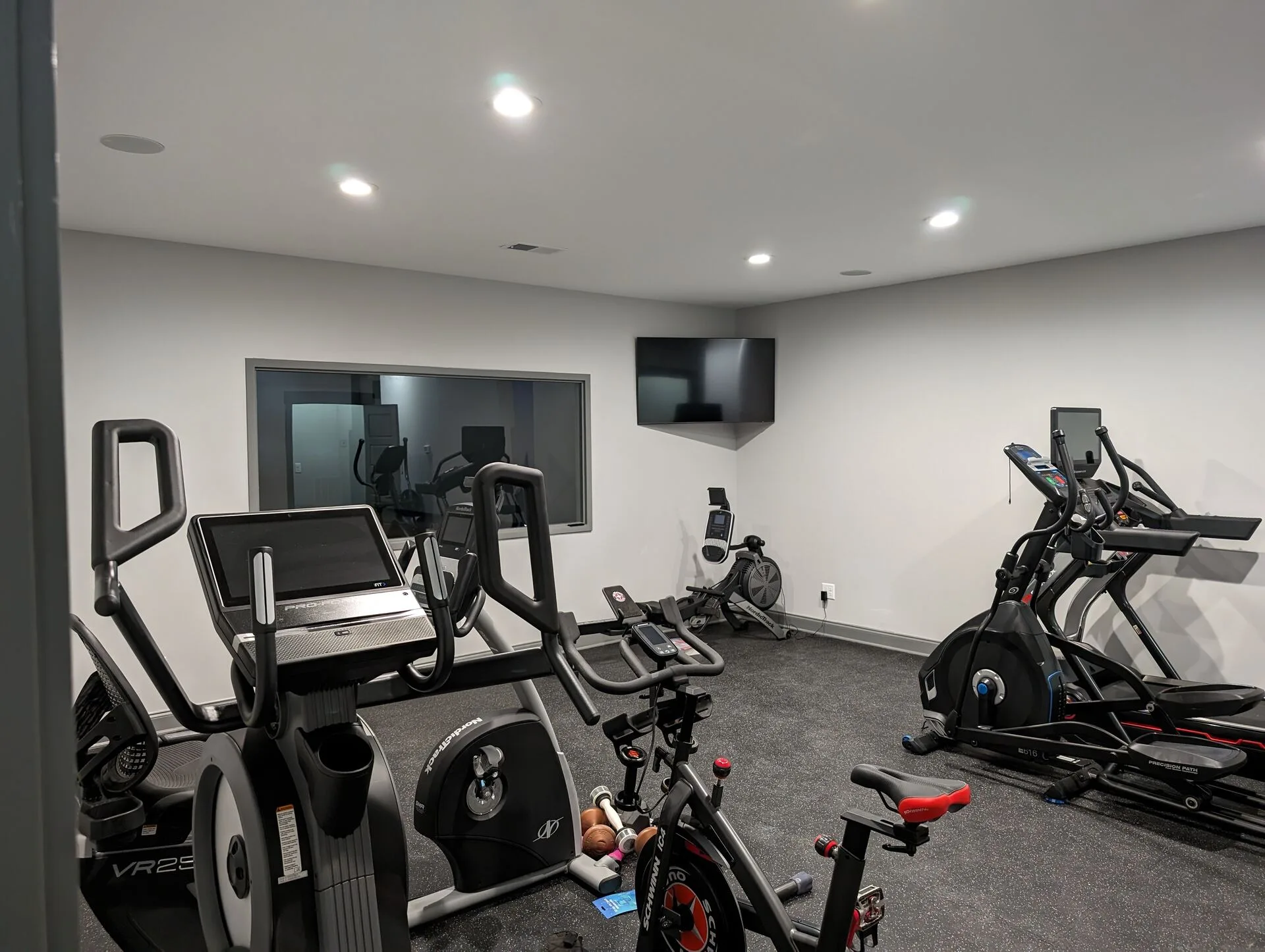 Private home fitness room with Peloton, elliptical, treadmill, and interior viewing window